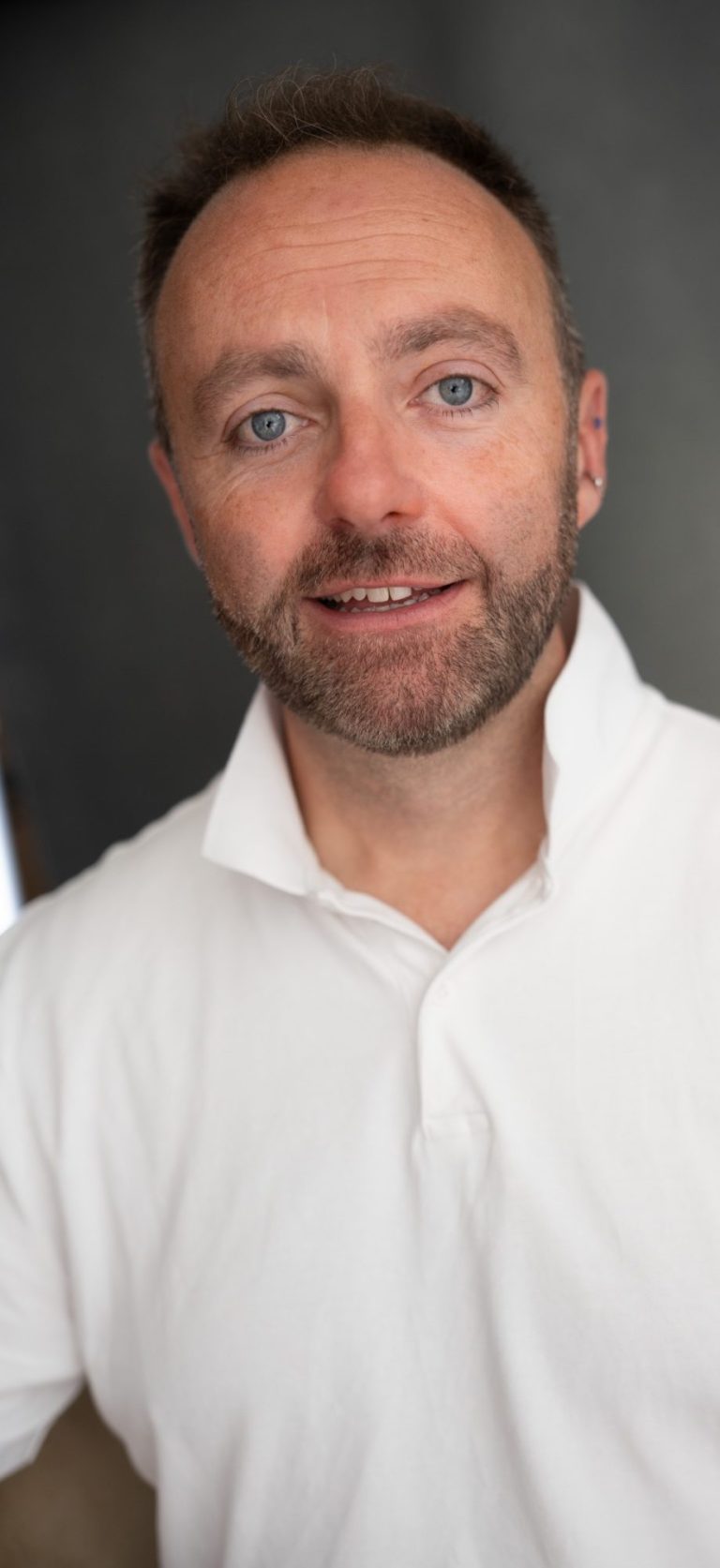 Jamie Read is a middle aged white man wearing a white T-shirt and smiling. He has short brown hair and a beard